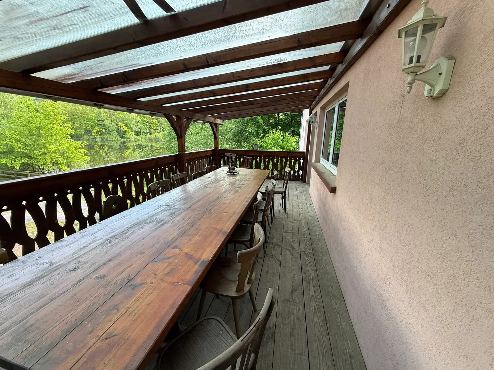 Vue d'angle de la terrasse avec la grande table en bois et lanterne murale