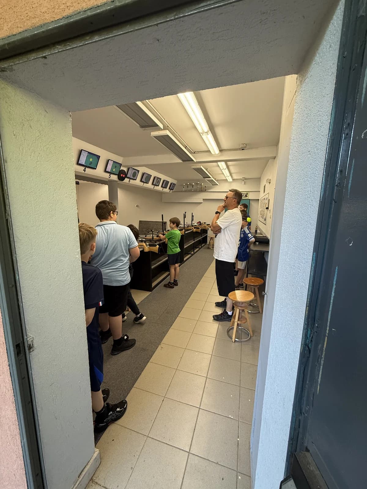 Séance d'école de tir au pas 10 m : un moniteur encadre des jeunes tireurs devant la ciblerie électronique du sous-sol