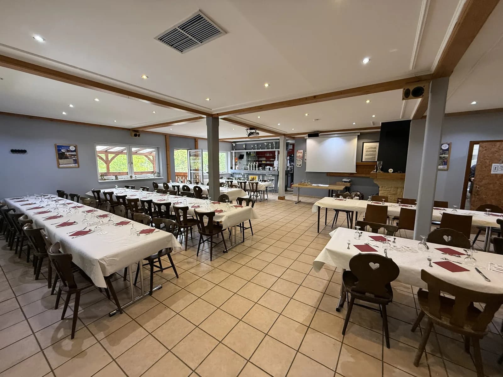 Salle polyvalente avec tables dressées pour un repas et bar au fond